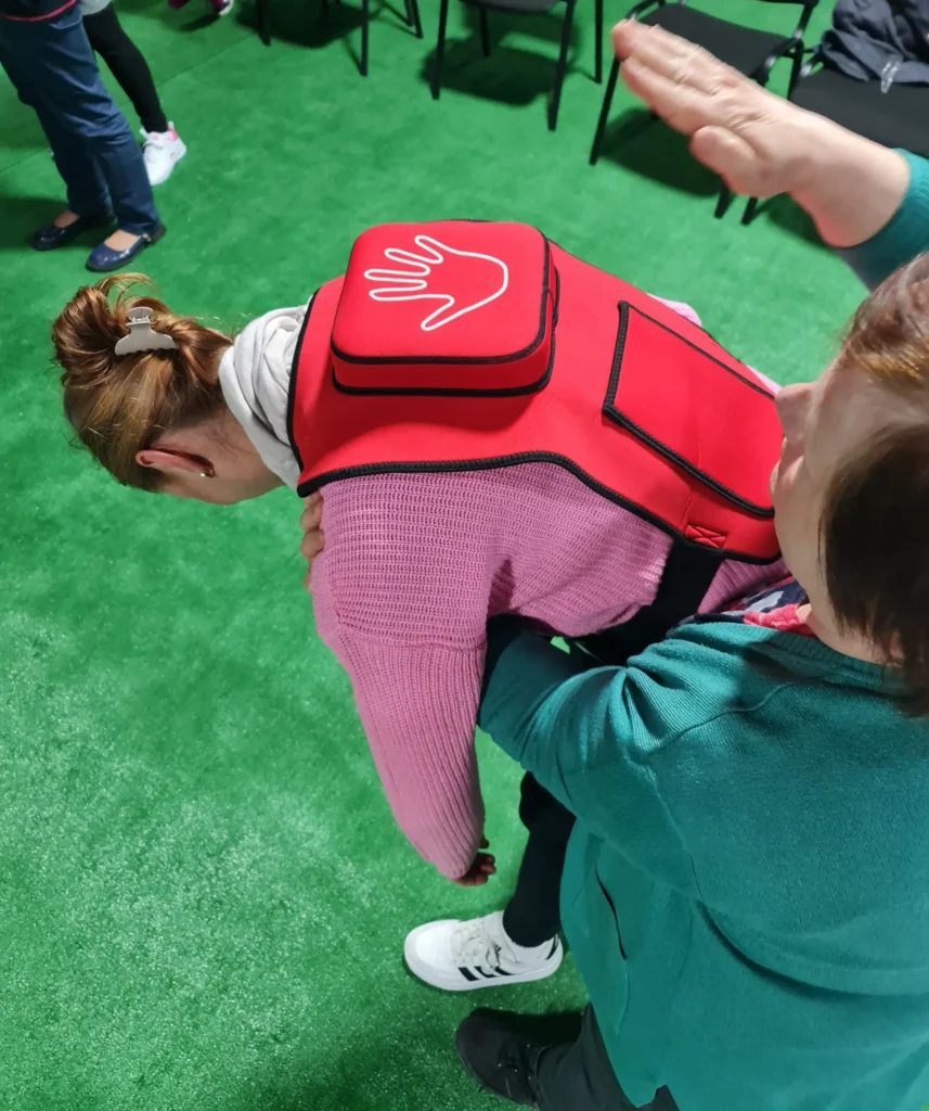 Uczestniczki szkolenia pierwszej pomocy ćwiczą pomoc osobie zadławionej z użyciem kamizelki treningowej